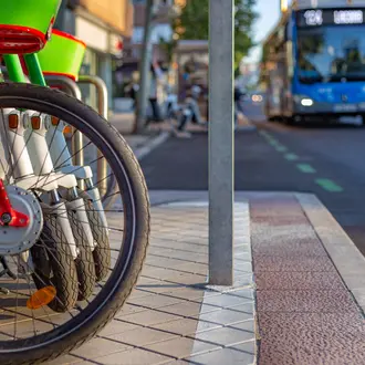 Rental bikes and scooters parked on sidewalk with bus on the road in background
