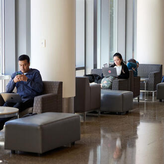 Chairs by the windows near the e62 cafe with a few students sitting and working