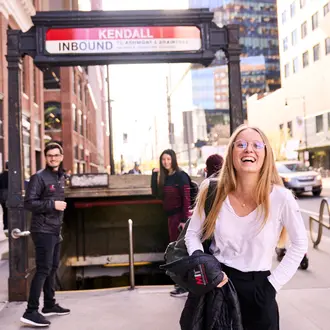 Three MIT Sloan students facing the camera with backs turned toward the MBTA station stairs outside in Kendall Square.