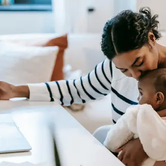 Image of a woman holding a baby in one arm and sitting near a computer