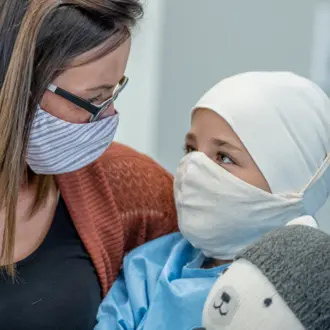 A mother hugs her young daughter while she receives cancer treatment