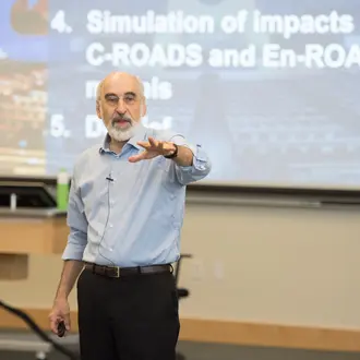 MIT Sloan Professor John Sterman in the classroom with a slide about the  C-ROADS and En-ROADS climate policy simulators behind him