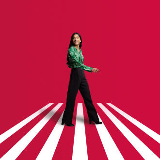 A woman in business wear walks across the frame with a red background with white stripes