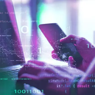 A person holds a mobile phone while typing on a computer, all overlayed with code and digital imagery