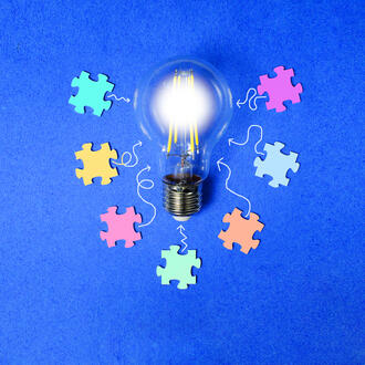 A lightbulb is surrounded by various colorful puzzle pieces