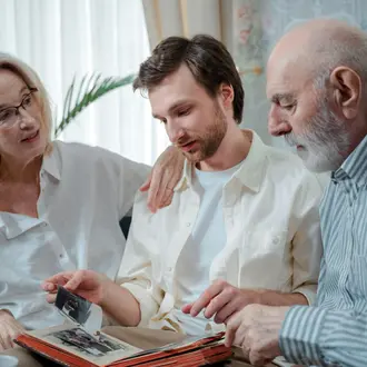 Image of an older man and woman with a young man who appears to be their son. They are looking at photos together.