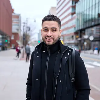 Mike Sanchez stands on a street in Cambridge and smiles at the camera