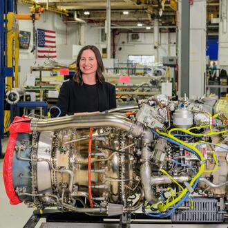 Sara Campbell EMBA '25 standing with a large engine in front of her