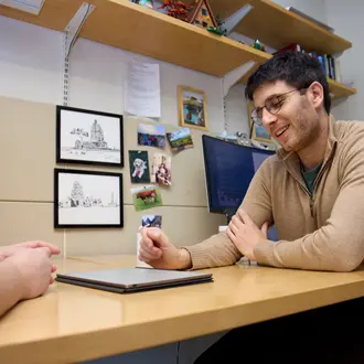 PhD student Ben Manning sits at a desk in the MIT Sloan PhD offices. He looks down at a tablet, talking to someone out of frame.