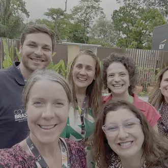 2 people smiling and 4 people smiling behind them posing for a selfie. 