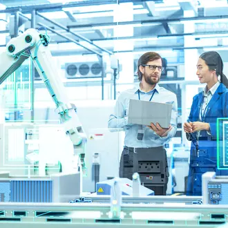 Employees in discussion inside a manufacturing plant with robotic arms and digital screens