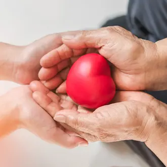 Two pairs of hands holding a red heart
