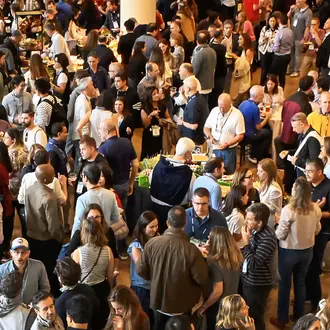 Large crowd gathers in a meeting space nearby banner that reads MIT Sloan Alumni Reunion