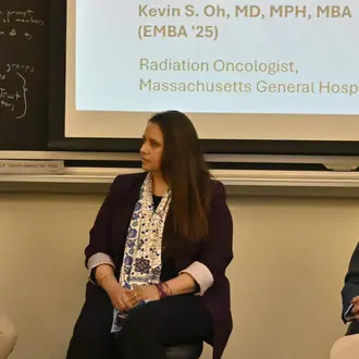Three people on a panel listen to a fourth panel member speak.