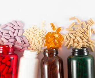 five brightly colored pill bottles on their sides with different sized pills spilling from each