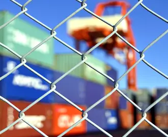 Photo of a container yard behind a chainlink fence to illustrate supply chain disruption.