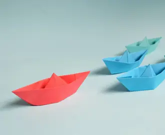 Paper origami boats on light blue background