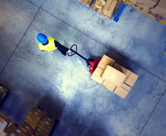 a warehouse worker pulls a wheeled pallet of boxes through a corridor