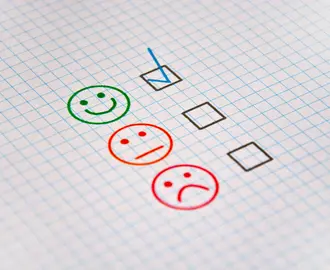 Happy, neutral, and sad faces on a piece of paper with checkboxes next to each, representing product rankings and consumer feedback.