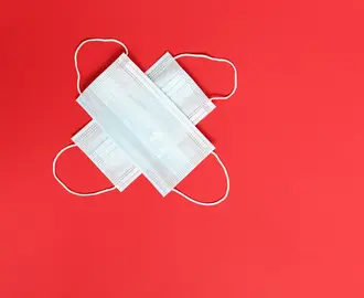 Two disposable COVID-19 face masks on an orange background