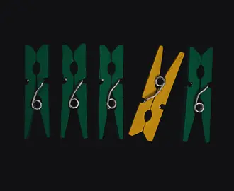 A yellow clothes pin among a row of green ones