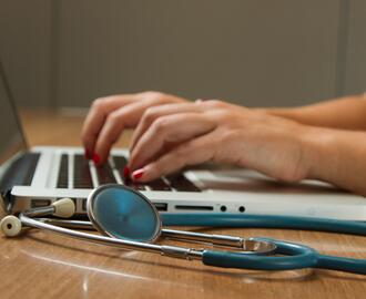 Hands with red nail polish typing on laptop with stethoscope next to it