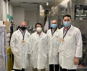 Three H-Lab students and Bayan Takizawa posing in lab coats at Continuus Pharmaceuticals