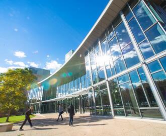 The outside of the MIT Sloan building E-62, on a sunny day with people walking near it