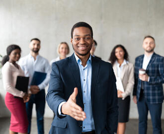 Business man extending his hand to you with a group of workers standing behind him