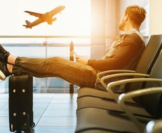 Man sitting in airport waiting area, staring out window at a plane taking off