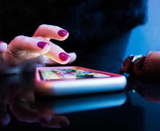 Hand with pink nail polish hovering over cell phone on table