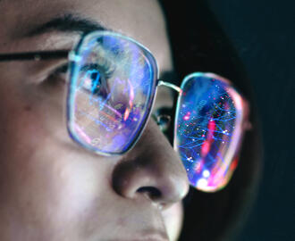 A person wears eyeglasses with lenses that reflect abstract digital art