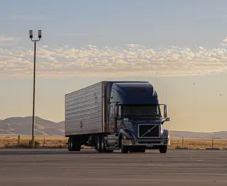 White freight truck on road with mountain range in the background.