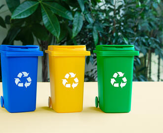 Three recycling bins in a row with leaves in the background