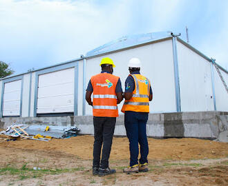 photograph of two men in high-vis vests and hard hats standning infront of a newly built warehouse