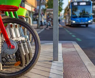 Rental bikes and scooters parked on sidewalk with bus on the road in background