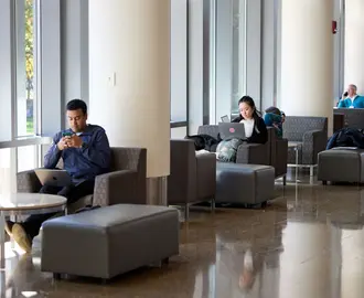 Chairs by the windows near the e62 cafe with a few students sitting and working