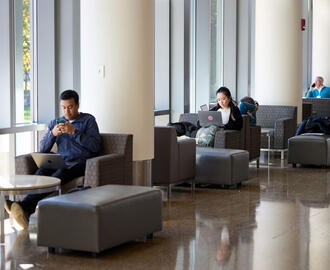 Chairs by the windows near the e62 cafe with a few students sitting and working