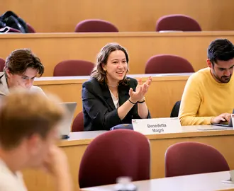 Female student speaking in class sitting between two students.