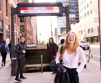 Three MIT Sloan students facing the camera with backs turned toward the MBTA station stairs outside in Kendall Square.