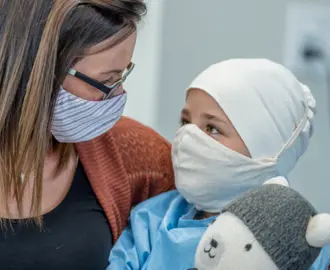 A mother hugs her young daughter while she receives cancer treatment