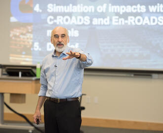 MIT Sloan Professor John Sterman in the classroom with a slide about the  C-ROADS and En-ROADS climate policy simulators behind him