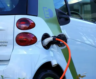 Image of the back of an electric car charging, with a charger and cord visible