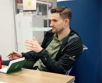 David Brown sits at a desk, talking to someone off camera. 