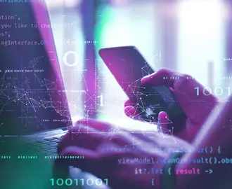A person holds a mobile phone while typing on a computer, all overlayed with code and digital imagery