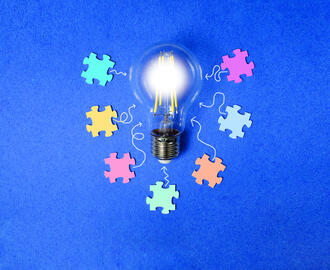 A lightbulb is surrounded by various colorful puzzle pieces