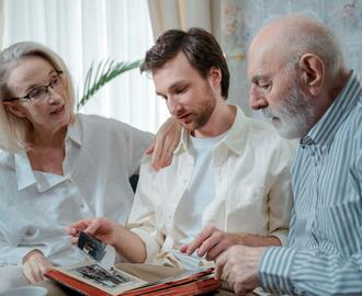 Image of an older man and woman with a young man who appears to be their son. They are looking at photos together.