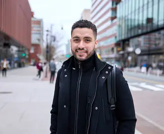 Mike Sanchez stands on a street in Cambridge and smiles at the camera