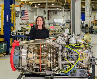 Sara Campbell EMBA '25 standing with a large engine in front of her