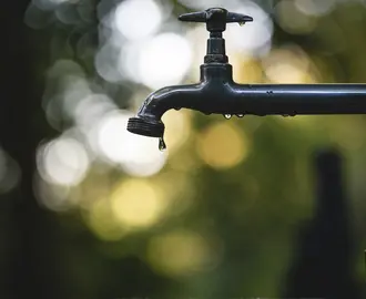 The image shows a water spigot with one drop falling out